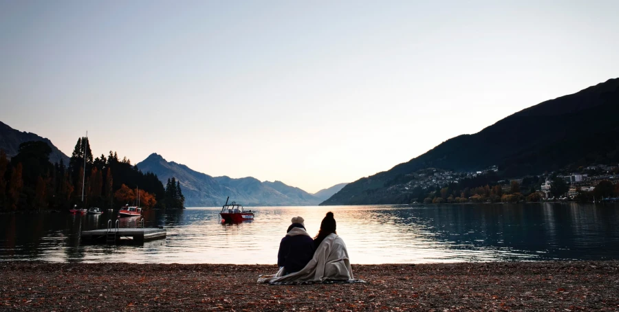 Friends sit on lakeside watching the sunset over Lake Whakatipu Queenstown near Te Pā Tāhuna